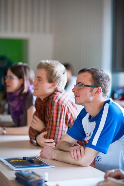 Ung, stilig collegestudent sitter i ett klassrum fullt av s — Stockfoto