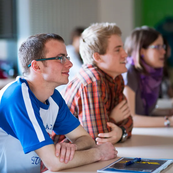 Ung, stilig collegestudent sitter i ett klassrum fullt av s — Stockfoto