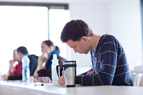 Joven, guapo estudiante universitario sentado en un salón de clases lleno —  Fotos de Stock