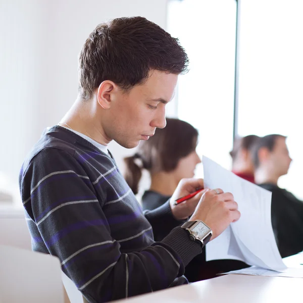 Ung, stilig hane högskolestudent som sitter i ett klassrum fullt — Stockfoto