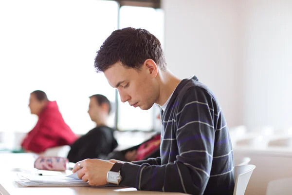 Fiatal, jóképű férfi főiskolai hallgató ül egy osztályteremben teljes — Stock Fotó