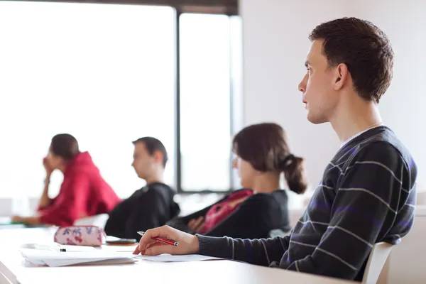 Young, handsome male college student sitting in a classroom full — Stock Photo, Image