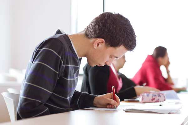 Young, handsome male college student sitting in a classroom full — Stock Photo, Image