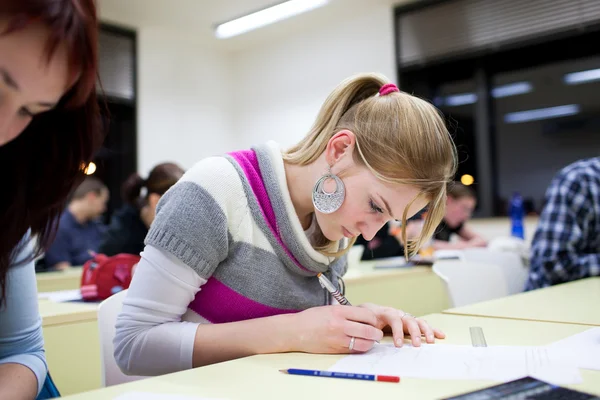 Linda estudiante universitaria sentada en un aula llena de estudiantes — Foto de Stock