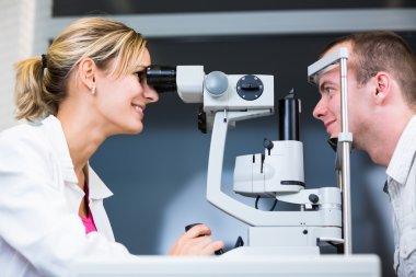 Optometry concept - handsome young man having her eyes examined clipart