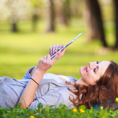 açık havada çok güzel bir bahar gününde bir parkta dinlenirken tablet bilgisayarını kullanan genç kadın