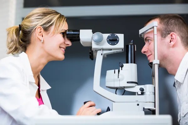 Optometrie concept - knappe jonge man met haar ogen onderzocht — Stockfoto