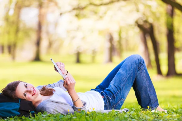 Νεαρή γυναίκα με τον υπολογιστή tablet ενώ χαλαρώνετε σε εξωτερικούς χώρους σε ένα πάρκο σε μια ανοιξιάτικη μέρα — Φωτογραφία Αρχείου