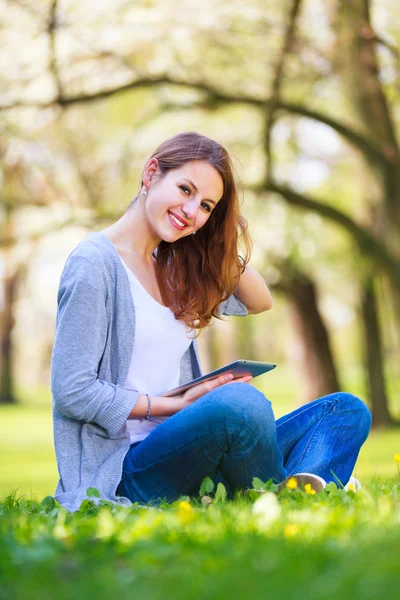 Jovem mulher usando seu computador tablet enquanto relaxa ao ar livre em — Fotografia de Stock