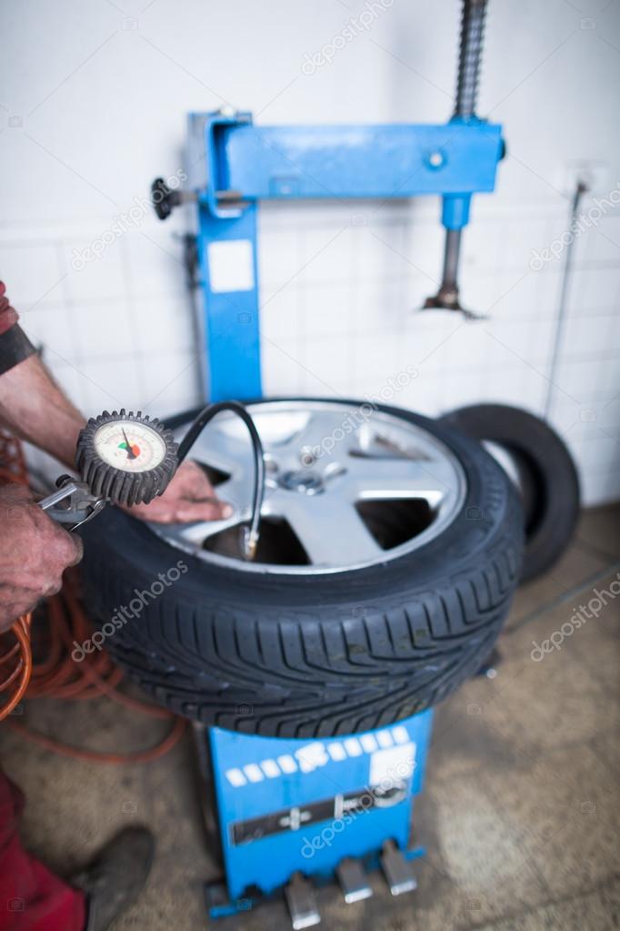 Auto mechanic in a garage checking the air pressure in a tyre wi