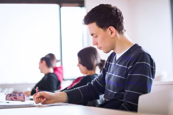 Młody, przystojny mężczyzna kolegium student siedzi w klasie — Zdjęcie stockowe