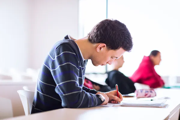 Młody, przystojny mężczyzna kolegium student siedzi w klasie — Zdjęcie stockowe