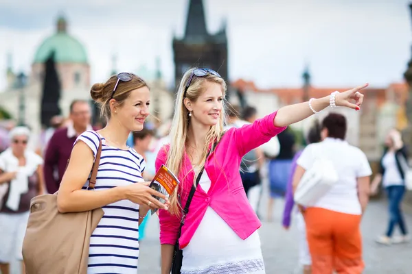 Две туристки, идущие вдоль Карлова моста во время осмотра достопримечательностей Праги — стоковое фото