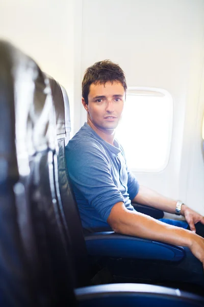 Joven guapo a bordo de un avión durante el vuelo, mira —  Fotos de Stock