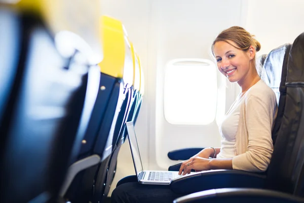 Jonge vrouw die werkt op haar laptopcomputer aan boord van een vliegtuig tijdens de vlucht — Stockfoto