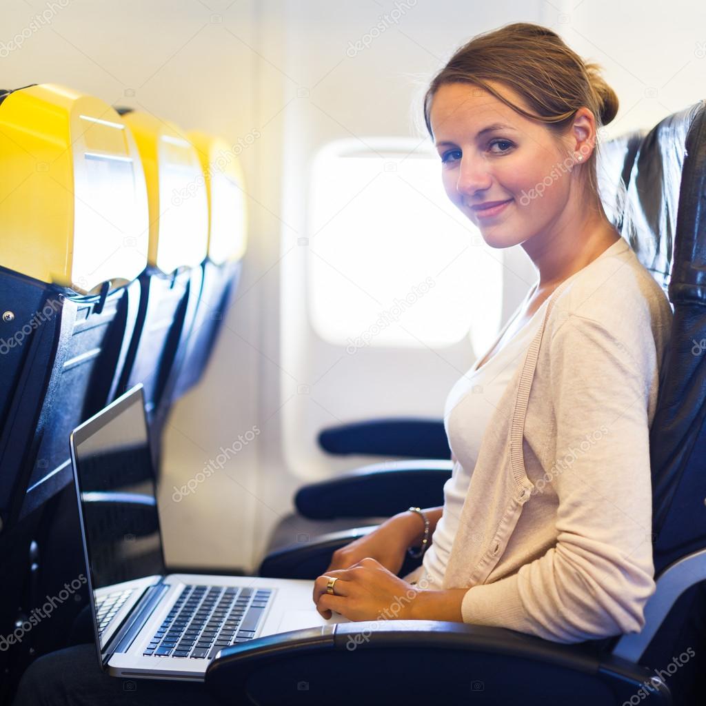 Young woman working on her laptop computer on board of an airplane during the flight