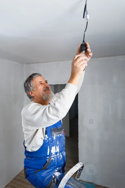 Homme âgé installant une ampoule dans un appartement récemment rénové i — Photo