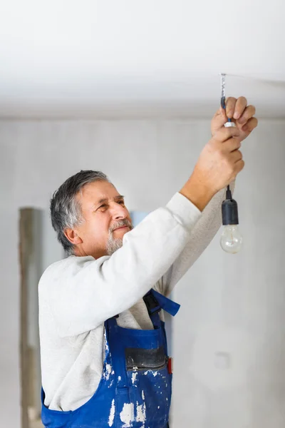 Uomo anziano che installa una lampadina in un appartamento appena ristrutturato i — Foto Stock