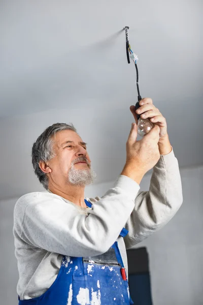 Hombre mayor instalando una bombilla en un apartamento recién renovado i — Foto de Stock