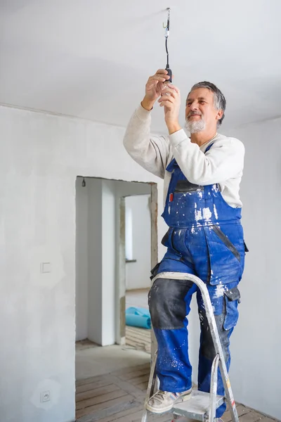 Senior man installing a bulb in a freshly renovated appartment i — Stock Photo, Image