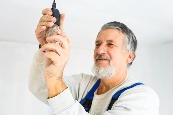 Hombre mayor instalando una bombilla en un apartamento recién renovado — Foto de Stock