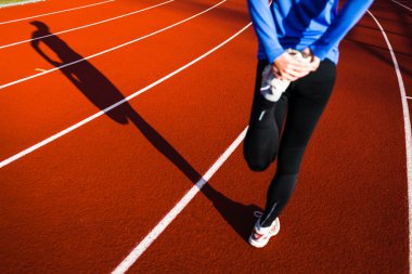 Young woman stretching before her run casts a shadow on the track clipart
