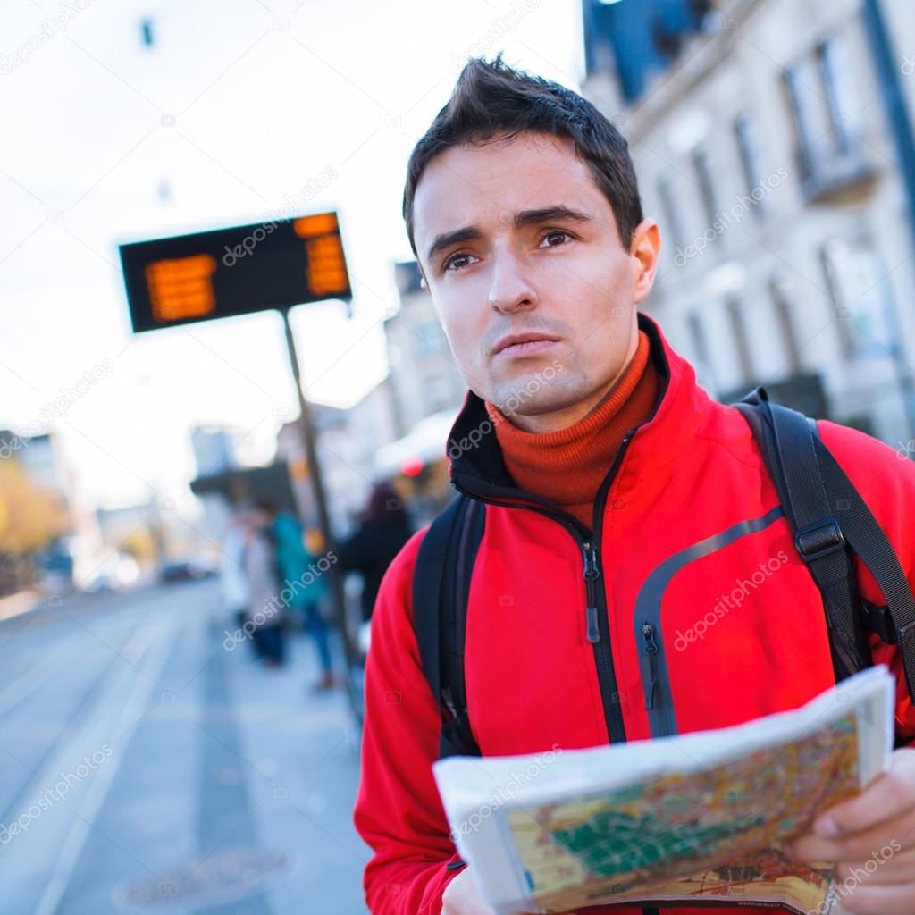Just arrived: handsome young man studying a map on a bus stop