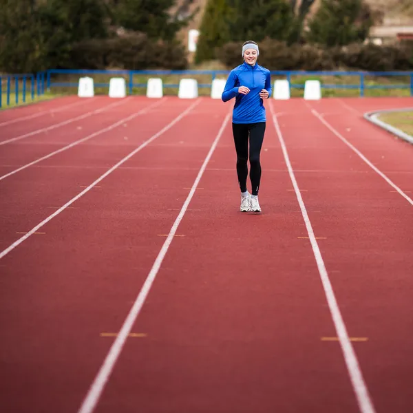 Mujer joven corriendo en un estadio de atletismo — Foto de Stock