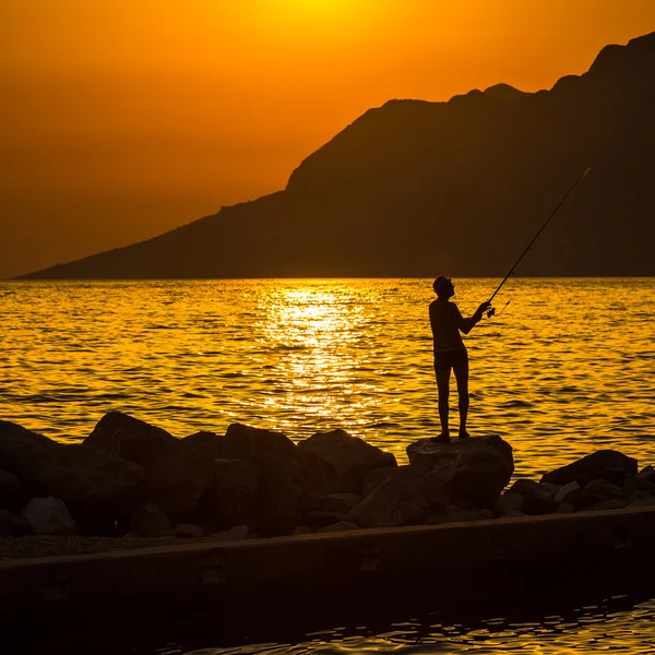 Silueta de pescador en la playa al atardecer colorido — Foto de Stock