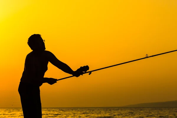 Silueta de pescador en la playa al atardecer colorido — Foto de Stock