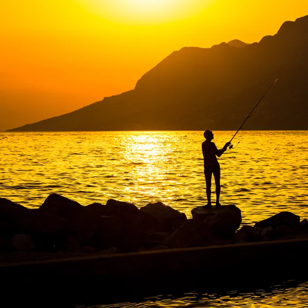Silueta de pescador en la playa al atardecer colorido — Foto de Stock