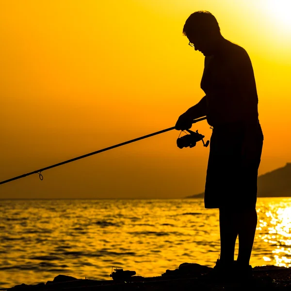 Silhouette de pêcheur sur la plage au coucher du soleil coloré — Photo