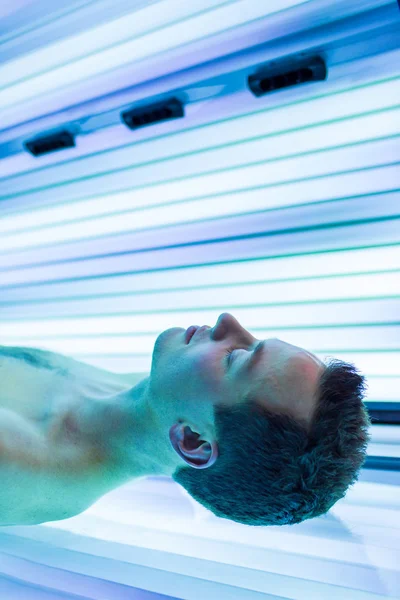 Beau jeune homme relaxant lors d'une séance de bronzage dans un moderne — Photo