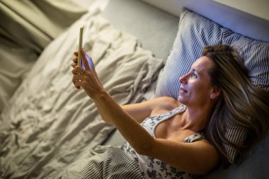 Güzel, orta yaşlı bir kadın akşamları yatmadan önce tabletini kullanıyor.