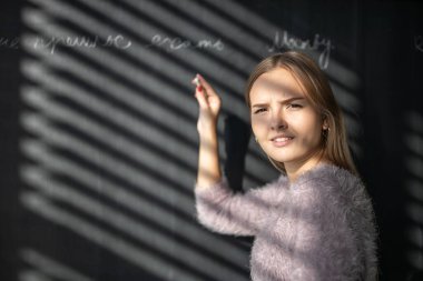 Güzel, genç bir kız öğrenci ders sırasında tahtası önünde.