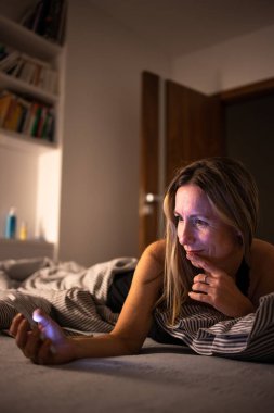 Güzel, orta yaşlı bir kadın uyumadan önce cep telefonunu evde kullanıyor.