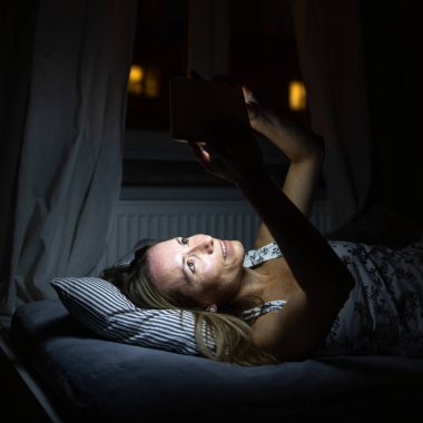 Orta yaşlı bir kadın, yatmadan önce tablet bilgisayarını kullanıyor. Uyumadan hemen önce mavi ışığa maruz kalıyor.