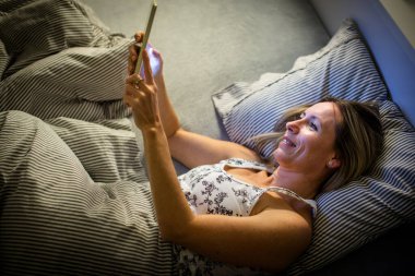 Güzel, orta yaşlı bir kadın akşamları yatmadan önce tabletini kullanıyor.