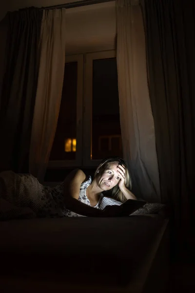 中年妇女晚上睡觉前在床上用平板电脑 睡觉前暴露在蓝光下 — 图库照片