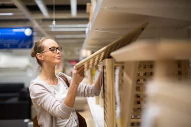 Güzel, genç bir kadın modern bir ev mobilyası mağazasında dairesi için doğru mobilyayı seçiyor (renk tonlu görüntü; sığ DOF)
