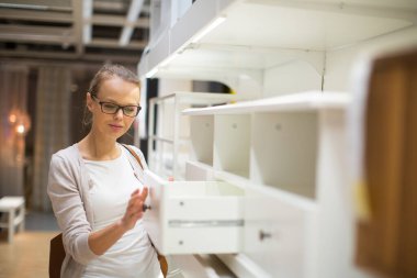 Güzel, genç bir kadın modern bir ev mobilyası mağazasında dairesi için doğru mobilyayı seçiyor (renk tonlu görüntü; sığ DOF)