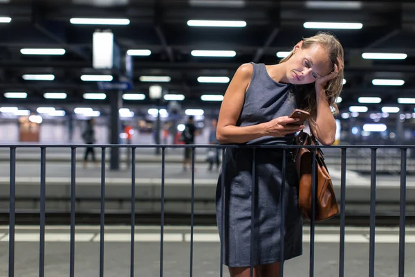 疲れて過労若い女性の通勤者モダンな駅に彼女の毎日の列車を待っている トーン カラー画像を待っている間彼女の携帯電話を使用して — ストック写真