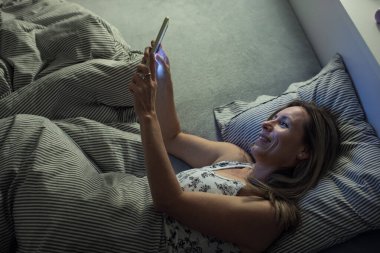 Güzel, orta yaşlı bir kadın akşamları yatmadan önce tabletini kullanıyor.