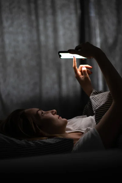 Jovem Mulher Cama Segurando Telefone Cansado Exausto Luz Azul Esticando — Fotografia de Stock
