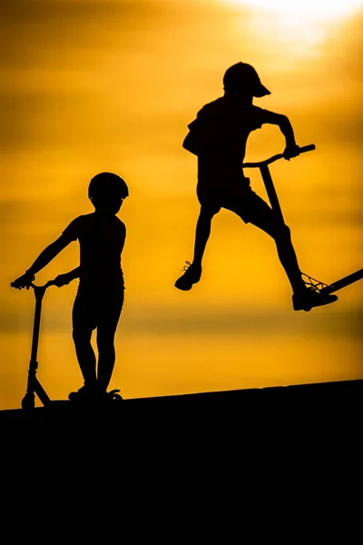 Silhuetas Menino Montando Uma Scooter Contra Fundo Pôr Sol Mar — Fotografia de Stock