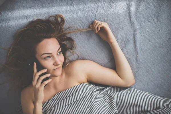Ładna Młoda Kobieta Łóżku Używa Smartfona Zamiast Się Zrelaksować — Zdjęcie stockowe