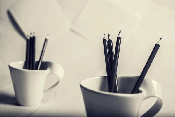 black and red pencils stand in two white cups in monochrome