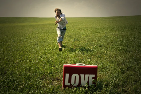 Man in het veld ziet er in koffer met het woord liefde — Stockfoto