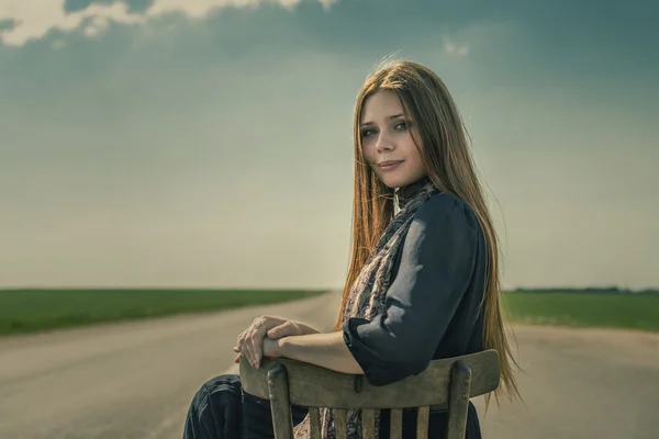 Uzun saçlı güzel kız açık havada yolda bir sandalyede oturuyor. — Stok fotoğraf