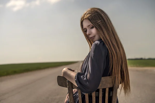 Piękna dziewczyna z długimi włosami na zewnątrz siedzi na krześle na drodze — Zdjęcie stockowe